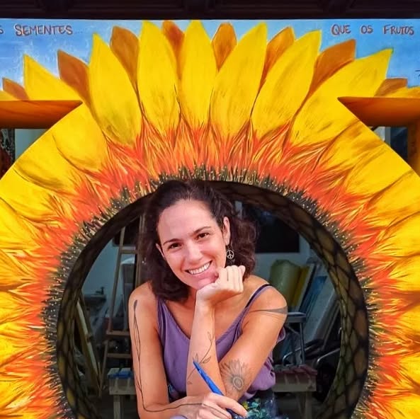 Michely sorrindo no centro de um girassol pintado em uma mureta