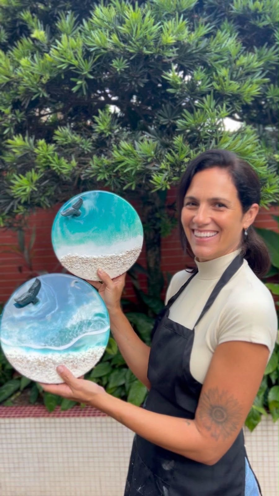 Michely segurando duas obras redondas de mar em resina